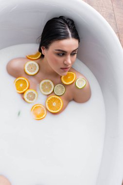 Genç bir kadın dilimlenmiş limon, limon ve portakalla süt banyosu yapıyor.