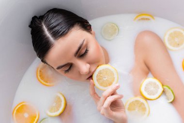 Süt banyosunda dinlenirken elinde limon dilimi tutan kadının genel görünümü