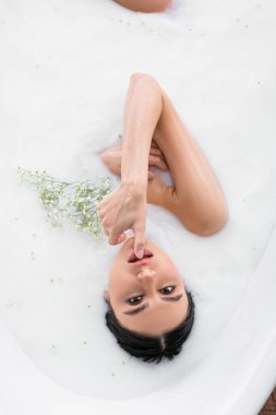 Cazibeli bir kadın sütle yıkanırken dudaklarına dokunuyor.