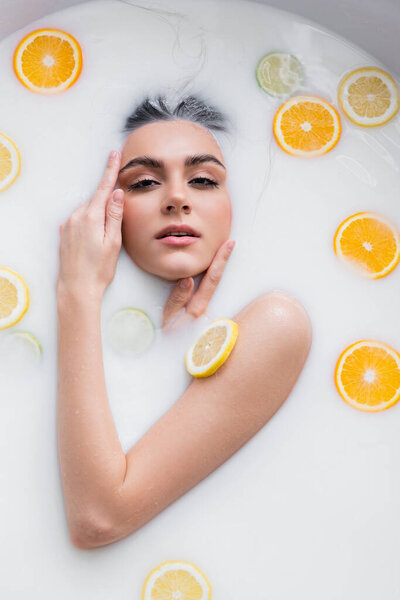 sensual woman looking at camera while bathing in milk with citrus slices