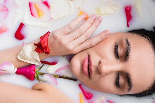 young woman with closed eyes relaxing in bath with milk and rose petals