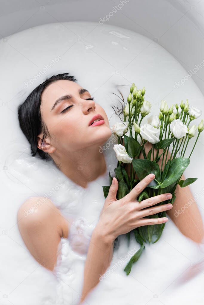pretty woman with closed eyes taking bath with milk and eustoma flowers