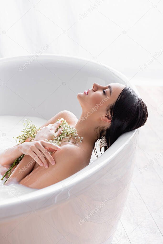 woman with closed eyes taking milk bath with gypsophila flowers