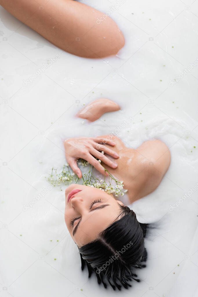 overhead view of young woman with white, tiny flowers enjoying milk bath