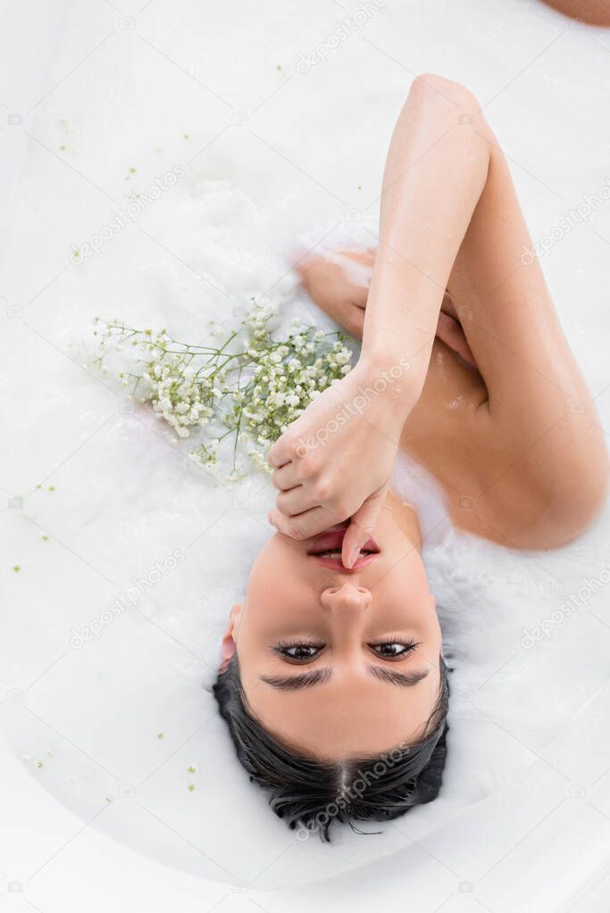 sensual woman looking at camera while taking milk bath with white, tiny flowers