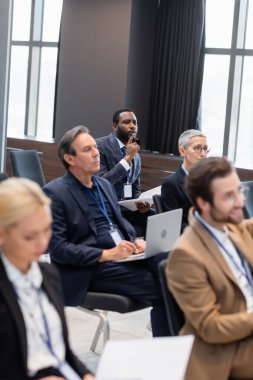 Odaklanmış Afrikalı Amerikalı iş adamı konferans odasında meslektaşlarının yanında oturuyor. 