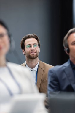 selective focus of young businessman in eyeglasses near blurred colleagues on seminar clipart