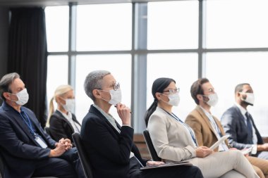 Tıp maskeli çok ırklı iş adamları konferans sırasında konferans odasında oturuyorlar.