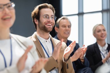 selective focus of young businessman applauding with multiethnic colleagues on seminar clipart