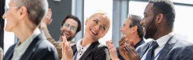selective focus of young businesswoman applauding together with interracial colleagues during seminar, banner clipart