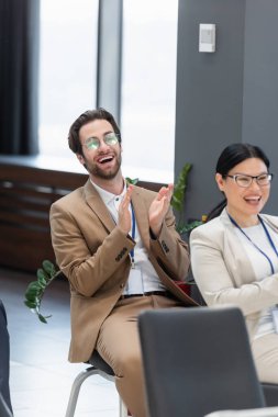 young businessman applauding near asian colleague during business conference clipart