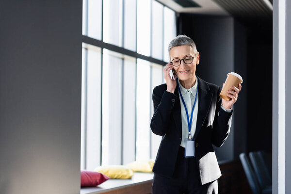 Mature businesswoman with coffee to go smiling and talking on smartphone 