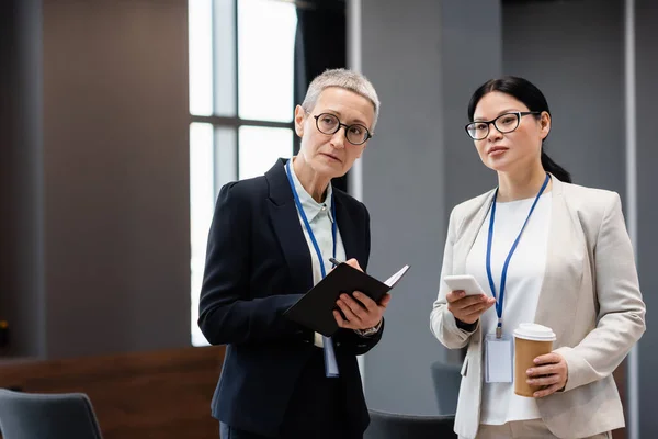 Interracial Businesswomen Smartphone Paper Cup Notebook Office — Stock Photo, Image