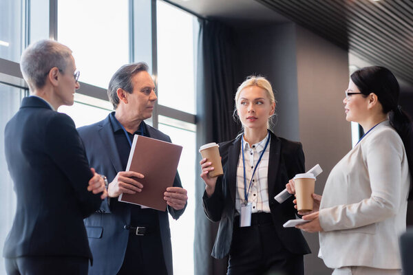 Interracial business people looking at colleague with digital tablet and takeaway drink 