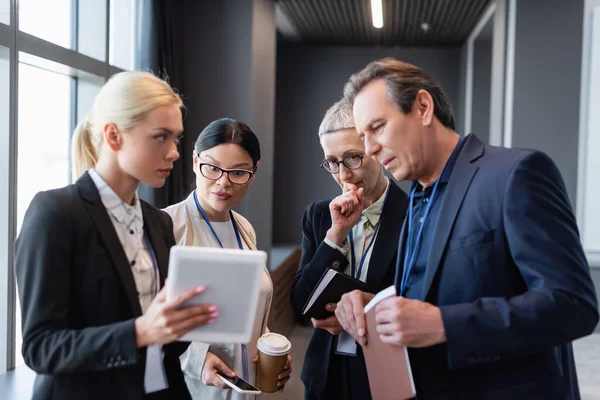 Interracial business people with paper folder and smartphone looking at blurred digital tablet