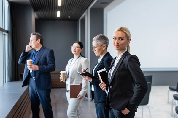 Businesswoman with digital tablet looking at camera near colleagues on blurred background 