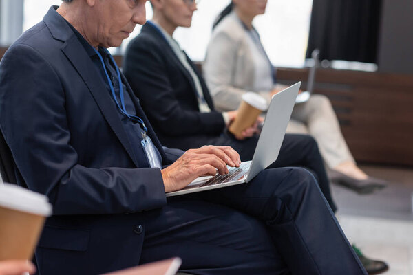 Cropped view of businessman using laptop near blurred colleagues during seminar 