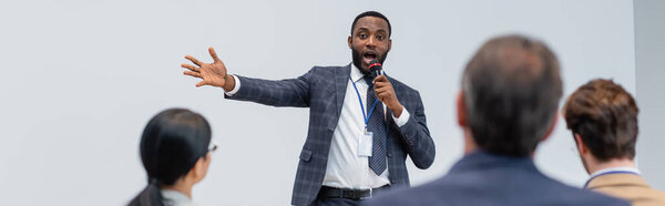 Африканский американский оратор с микрофоном разговаривает рядом размытые деловые люди, баннер 
