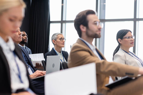 Зрелая деловая женщина, которая отворачивается от многонациональных коллег во время семинара 