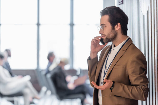 Side view of young businessman talking on mobile phone near conference room 