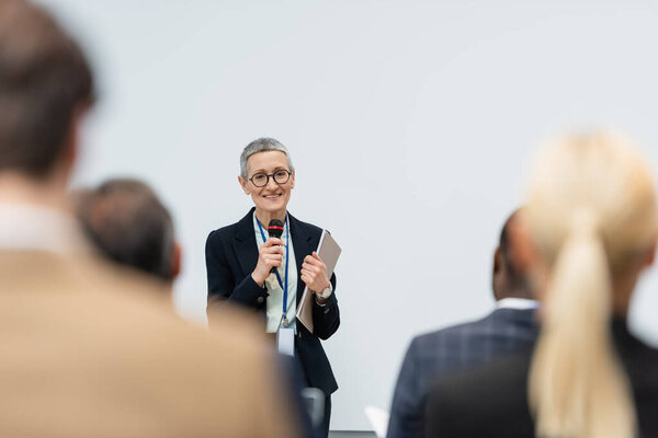 Cheerful middle aged speaker with paper folder talking during business meeting 