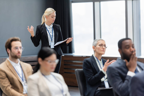 Businesswoman with paper folder talking near multiethnic colleagues in conference room 