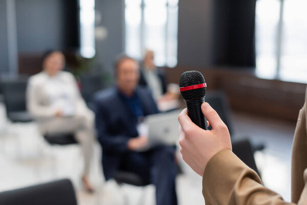 speaker holding microphone near blurred participants during business conference