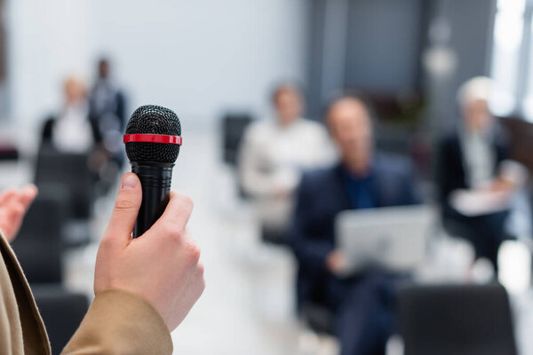 speaker holding microphone near blurred business people during seminar