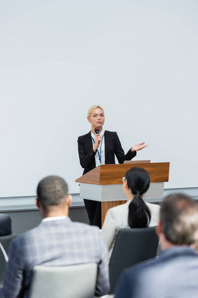 back view of audience near lecturer pointing with hand while speaking in microphone during seminar