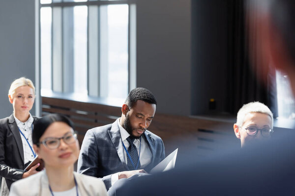 мультикультурные участники сидят в конференц-зале рядом с лектором на размытом переднем плане