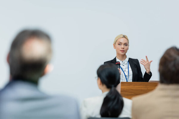 young speaker gesturing while talking to blurred business people during seminar