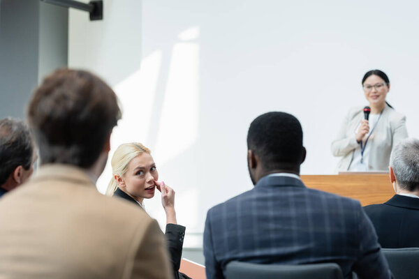 молодая женщина разговаривает с коллегами во время семинара у преподавателя азиатского языка на размытом фоне