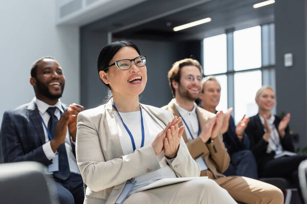Азиатская предпринимательница аплодирует во время семинара вблизи размытых межрасовых коллег