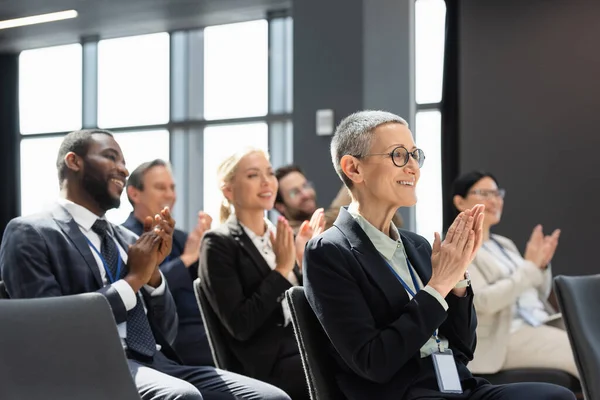 joyful multicultural business people applauding during seminar, blurred background
