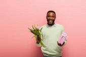 veselý africký Američan s dárkové krabice a tulipány smějící se na kameru na růžovém pozadí