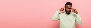 Kafası karışmış Afrikalı Amerikalı adam pembe arka planı işaret ediyor. 