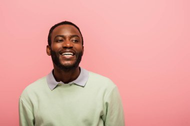 Gülümseyen Afro-Amerikan adam pembe üzerine inzivaya çekilmiş bakışlarını kaçırıyor. 