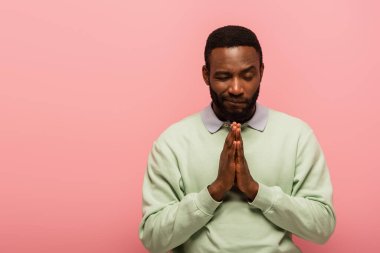 African american man standing with praying hands isolated on pink  clipart