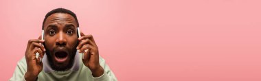 Shocked african american man talking on smartphones isolated on pink with copy space, banner  clipart
