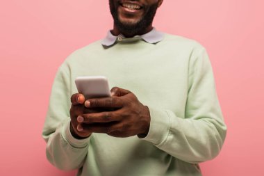 Arkaplanı bulanık, pembe renkli, gülümseyen Afro-Amerikan bir adamın ellerinde akıllı telefon görüntüsü. 