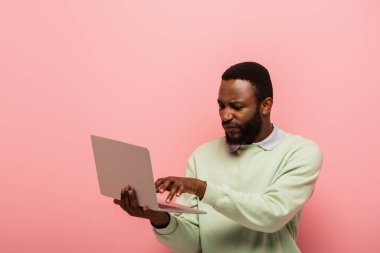 Pembe dizüstü bilgisayar kullanan hoşnutsuz Afro-Amerikan bir adam.