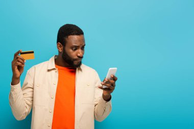 Düşünceli Afrikalı Amerikalı adam cep telefonuna bakarken elinde mavi kart tutuyor.