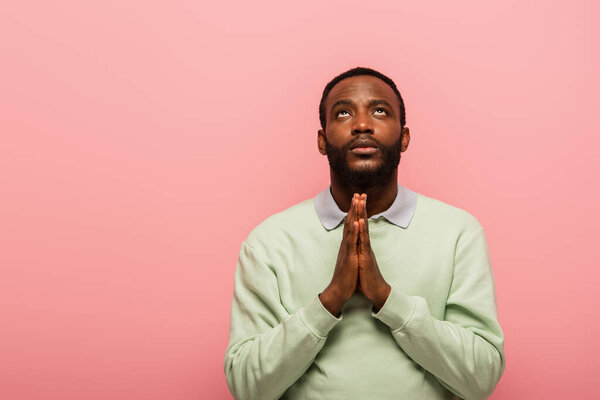 African american man with praying hands looking up isolated on pink 
