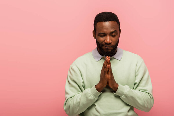 African american man standing with praying hands isolated on pink 