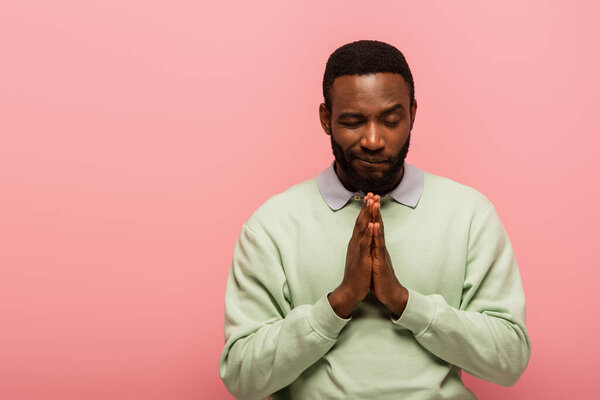 Африканский американец, стоящий с молящимися руками, изолированный на розовом 