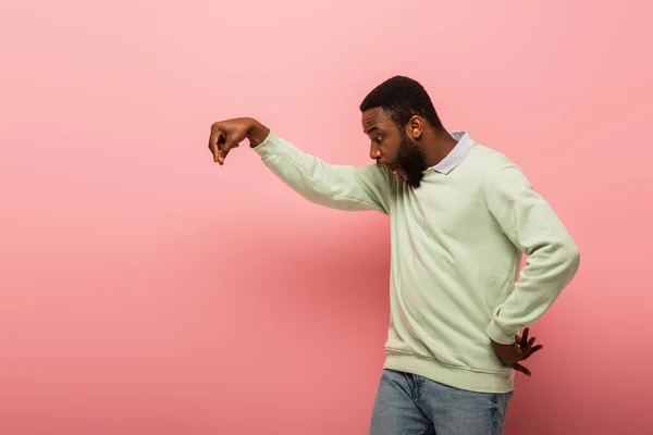 ピンクの背景に何かを持っているショックを受けたアフリカ系アメリカ人男性 — ストック写真