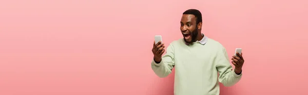 ピンクの背景にスマートフォンを持つ正のアフリカ系アメリカ人男性 バナー — ストック写真