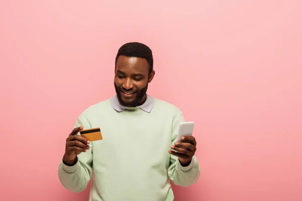 Afrykański Amerykanin Pomocą Smartfona Karty Kredytowej Różowym Tle — Zdjęcie stockowe