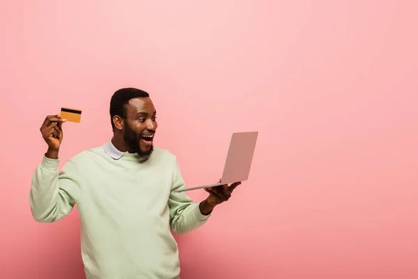 Hombre Afroamericano Asombrado Sosteniendo Tarjeta Crédito Portátil Sobre Fondo Rosa —  Fotos de Stock