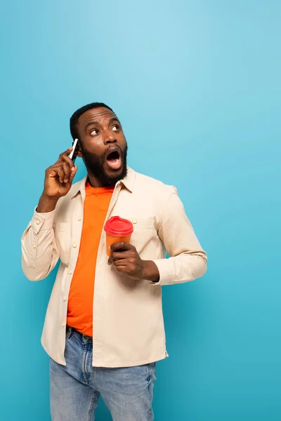 Шокированный Африканский Американец Кофе Пойти Говорить Мобильному Телефону Изолированы Синий — стоковое фото